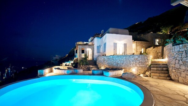 A swimming pool surrounded by stone walls and steps leading to a building with a lighted entrance.