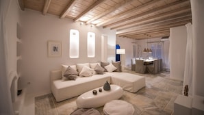 A modern living room with a wooden ceiling, a sofa set, a coffee table, and a dining area in the background.