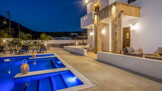 Una casa moderna con piscina, mobiliario de exterior y fachada de piedra.
