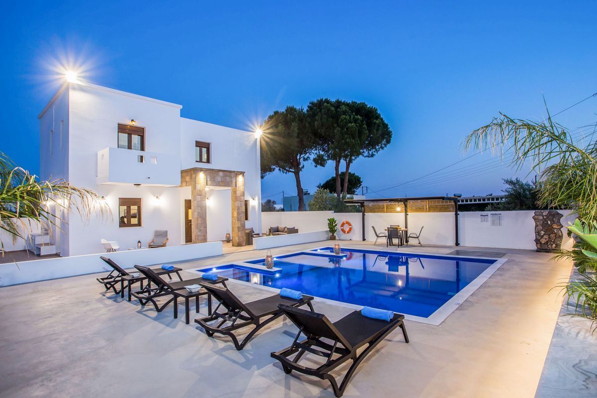 Eine moderne Villa mit Swimmingpool, Liegestühlen und einem gut beleuchteten Außenbereich.