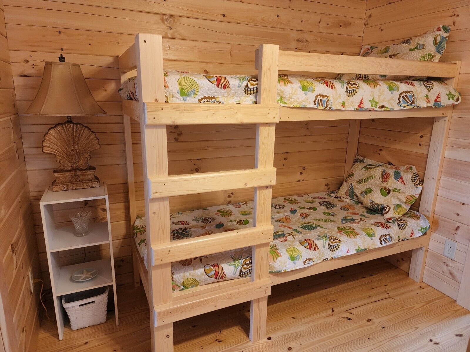 Ein Stockbett mit einer verzierten Muschel am Kopfteil, einer kleinen Ablage mit einer Glasvase und einem Korb darunter.