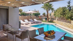 Ein Poolbereich mit Korbmöbeln, einem Tisch mit Obstschale und Blick auf den Pool und die umliegende Landschaft.