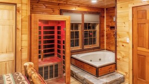 Interior de una cabaña de madera con baño de piso de piedra, un banco de madera y una sauna roja.