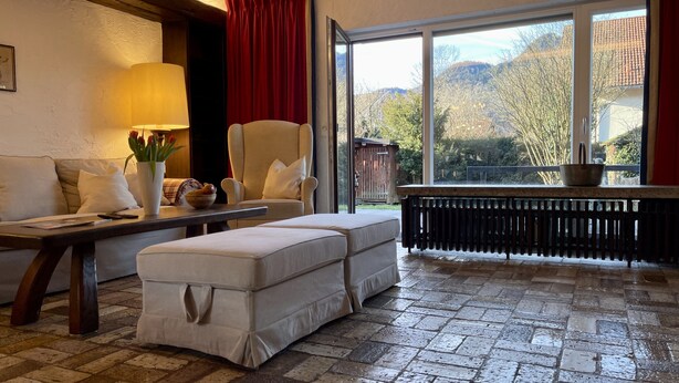 A cozy room with a sofa, a table with a lamp, a window with a view of trees and mountains, and a radiator. - Spacious family apartment with a sauna, fireplace, garden, and terrace near Brauneck (Lenggries)