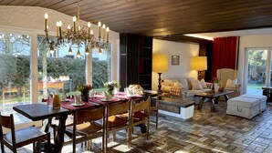A dining area with a wooden table and chairs, a chandelier, and a view of the outdoors. - Spacious family apartment with a sauna, fireplace, garden, and terrace near Brauneck (Lenggries)