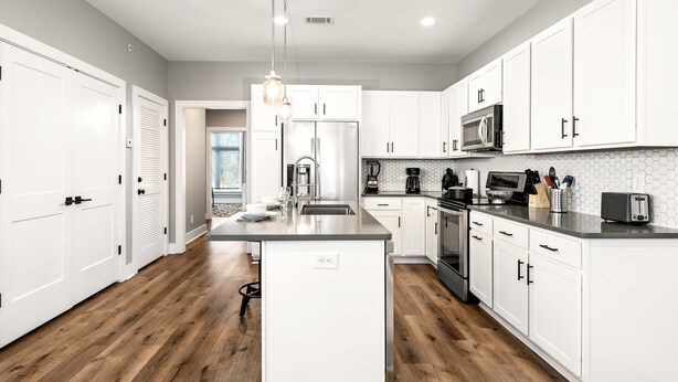A modern kitchen with white cabinets, a central island, stainless steel appliances, and a wooden floor.