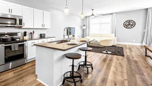 A modern kitchen with white cabinets, a central island with stools, stainless steel appliances, and pendant lighting.