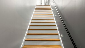 A staircase with wooden steps and a black handrail, leading upwards.