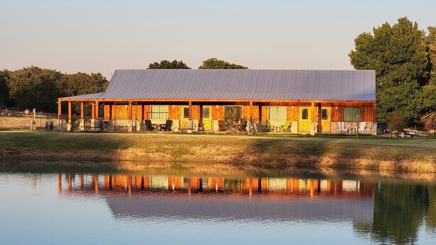 A rustic building with a metal roof, wooden walls, and a reflection in the water. - Safari Cabana at Tipsy Toad Retreat (Boyd)