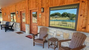 A covered porch with wooden walls and large windows overlooking a grassy area. - Safari Cabana at Tipsy Toad Retreat (Boyd)
