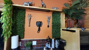 A reception area with a wooden counter, a green wall with animal decorations, a hanging plant, and a coffee machine. - Safari Cabana at Tipsy Toad Retreat (Boyd)