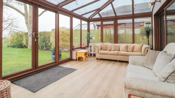 A conservatory with a glass roof, a beige sofa, and a small table with a plant. - Morgan House (Bridgwater)