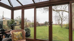 A conservatory with a stationary bike, wicker chair, and a view of a grassy backyard. - Morgan House (Bridgwater)