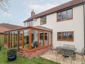 A house with a glass conservatory, a patio with a table and chairs, and a brick wall. - Morgan House (Bridgwater)