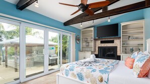 A bedroom with a large bed, a ceiling fan, a TV, and a fireplace. - Waterfront - 5 BR, 4 BA, Pool w Tub, 80' Dock, Tiki Hut, Beach Nearby, Parking (Marathon)