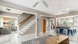 A spacious living area with a staircase, a kitchen with bar stools, and a ceiling fan. - Waterfront - 5 BR, 4 BA, Pool w Tub, 80' Dock, Tiki Hut, Beach Nearby, Parking (Marathon)