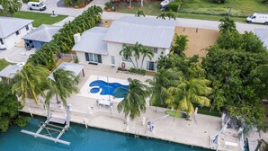 An aerial view of a residential property with a swimming pool, a dock, and a well-maintained lawn. - Waterfront - 5 BR, 4 BA, Pool w Tub, 80' Dock, Tiki Hut, Beach Nearby, Parking (Marathon)