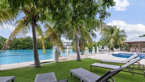 A poolside area with lounge chairs, palm trees, and a clear view of the pool. - Waterfront - 5 BR, 4 BA, Pool w Tub, 80' Dock, Tiki Hut, Beach Nearby, Parking (Marathon)