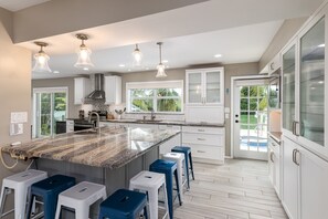 Een moderne keuken met een groot eiland, witte kastjes en uitzicht op het buiten.