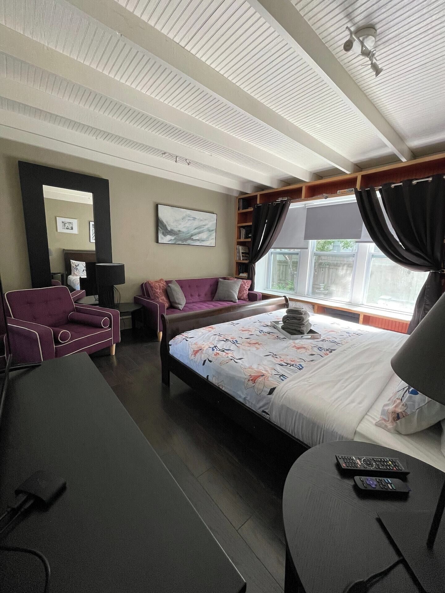 Ein Hotelzimmer mit einem Bett, einem Schlafsofa, einem Schreibtisch, einem Stuhl, einem Bücherregal und einem großen Fenster mit Vorhängen.