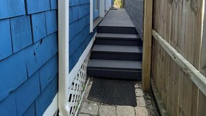A narrow pathway leading to a wooden door, flanked by blue siding and a wooden fence. - Old Town “Secret Chef”,  near Historic Downtown Saint Augustine (St. Augustine)