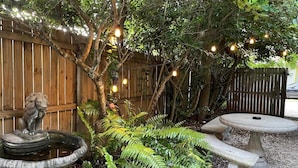 A garden with a stone fountain, a wooden fence, and string lights. - Old Town “Secret Chef”,  near Historic Downtown Saint Augustine (St. Augustine)