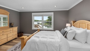 Une chambre à coucher avec un grand lit, une commode, une fenêtre donnant sur un beau paysage et une table de chevet avec une lampe.