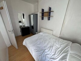 A bedroom with a bed, a wardrobe, a mirror, and a shelf unit.