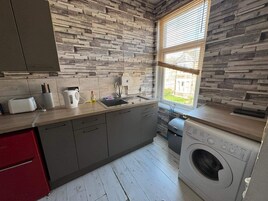 Una cocina con protector contra salpicaduras de pared de piedra, una ventana, una lavadora y un armario rojo.