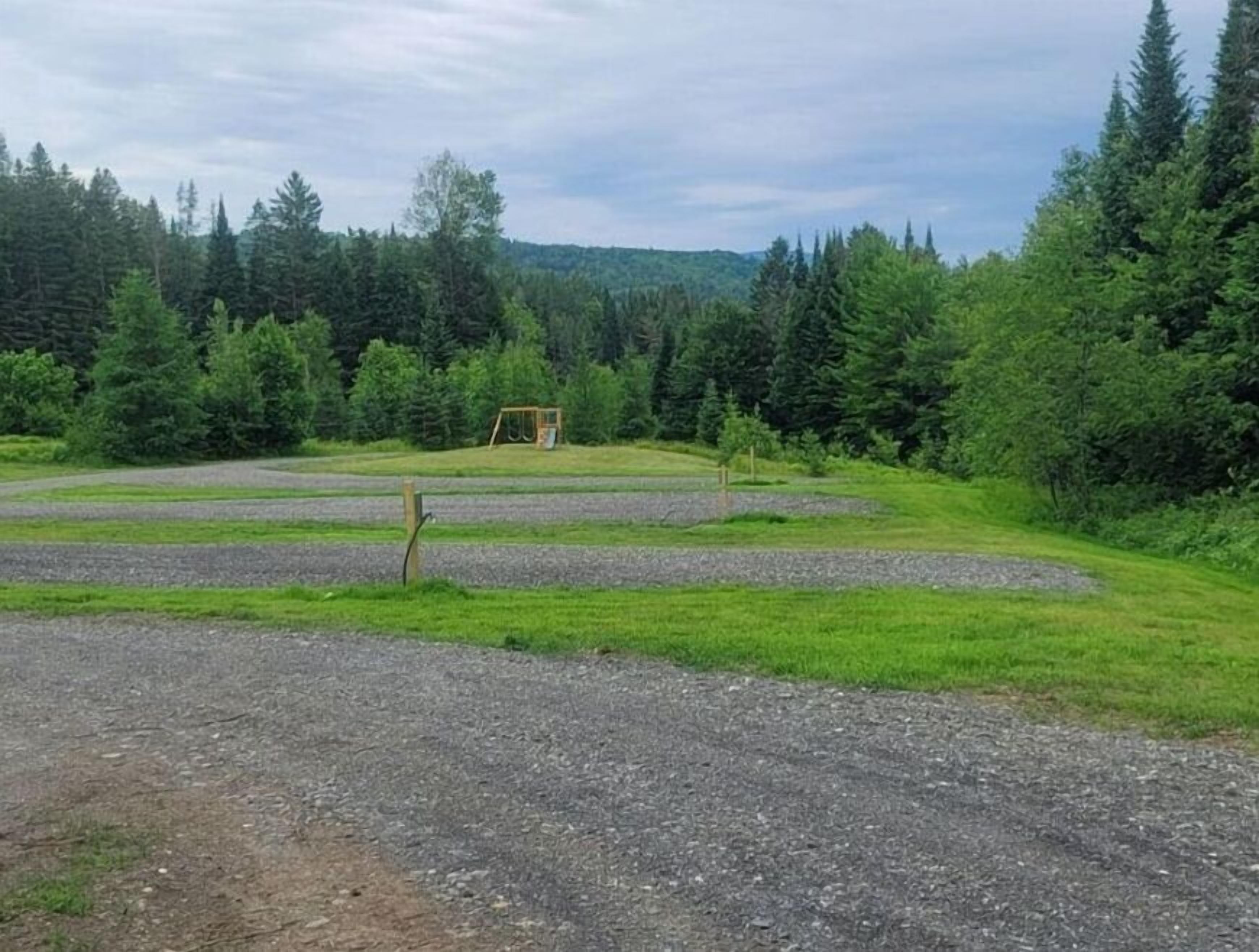 En parkingsplads med grus og et gyngestativ i en skov.