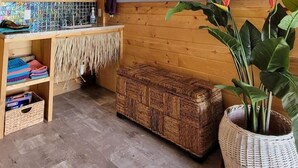Una habitación con un banco de madera, una cesta tejida, una planta grande en maceta, un televisor de pared y una estantería con toallas y un espejo.
