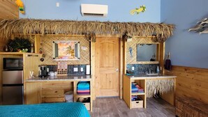 Una habitación con kitchenette, una cama y un techo de paja.