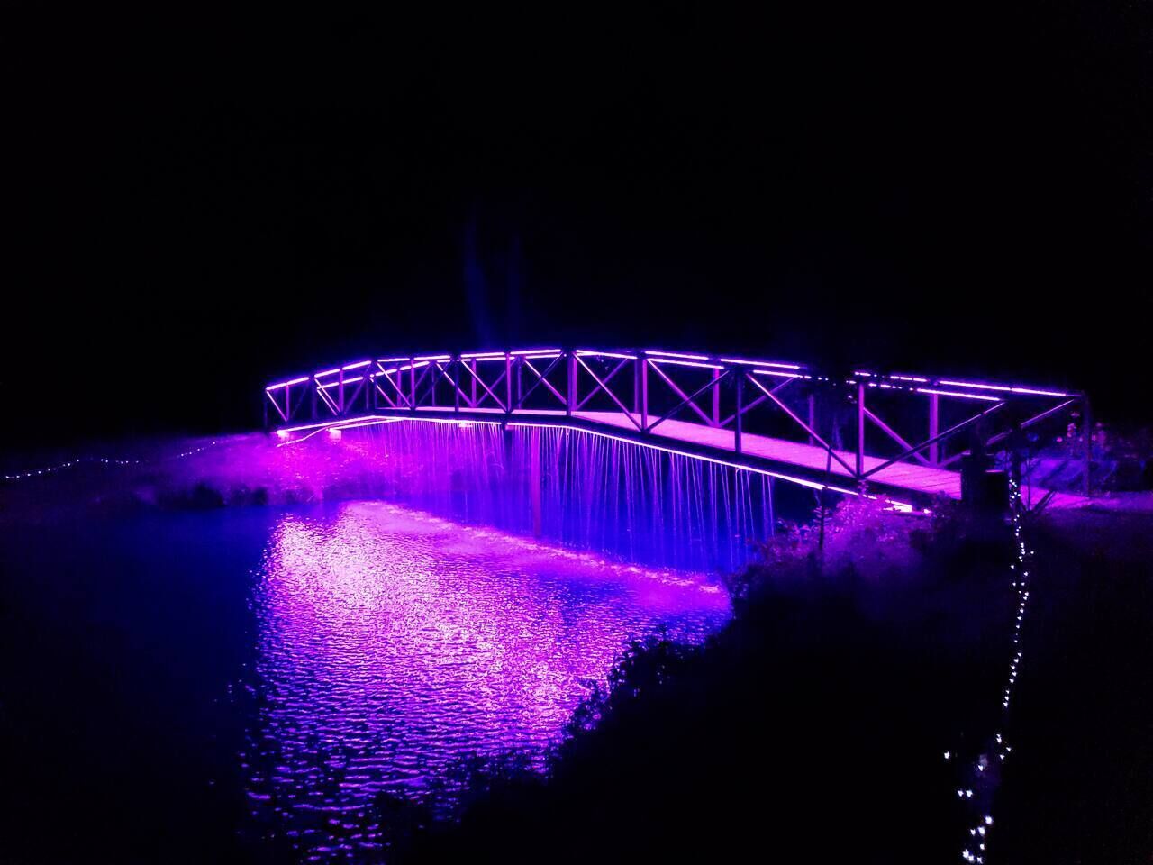 Eine Brücke, beleuchtet mit violettem Licht, über einem Gewässer.