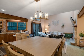 A modern kitchen with a dining area, wooden cabinets, and a chandelier.