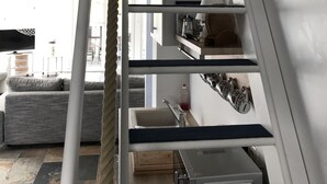A modern interior with a white staircase, a kitchen area, and a living room with a sofa and a TV.