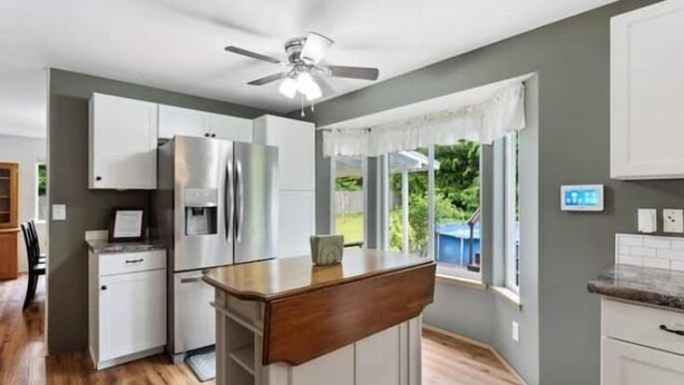 A modern kitchen with white cabinets, a stainless steel refrigerator, a wooden island, and a ceiling fan. - Spacious , RV parking, yard, cozy fireplaces, game library, near Manchester (Port Orchard)