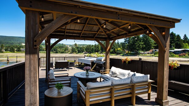 A wooden deck with a covered seating area, a barbecue grill, and a view of the surrounding landscape. - The Spot at Porpoise Bay (Sechelt)