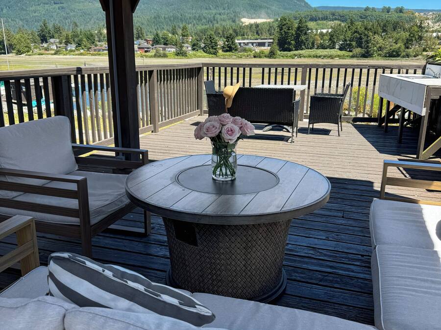 A covered outdoor seating area with a round table, cushioned seating, and a vase of flowers.
