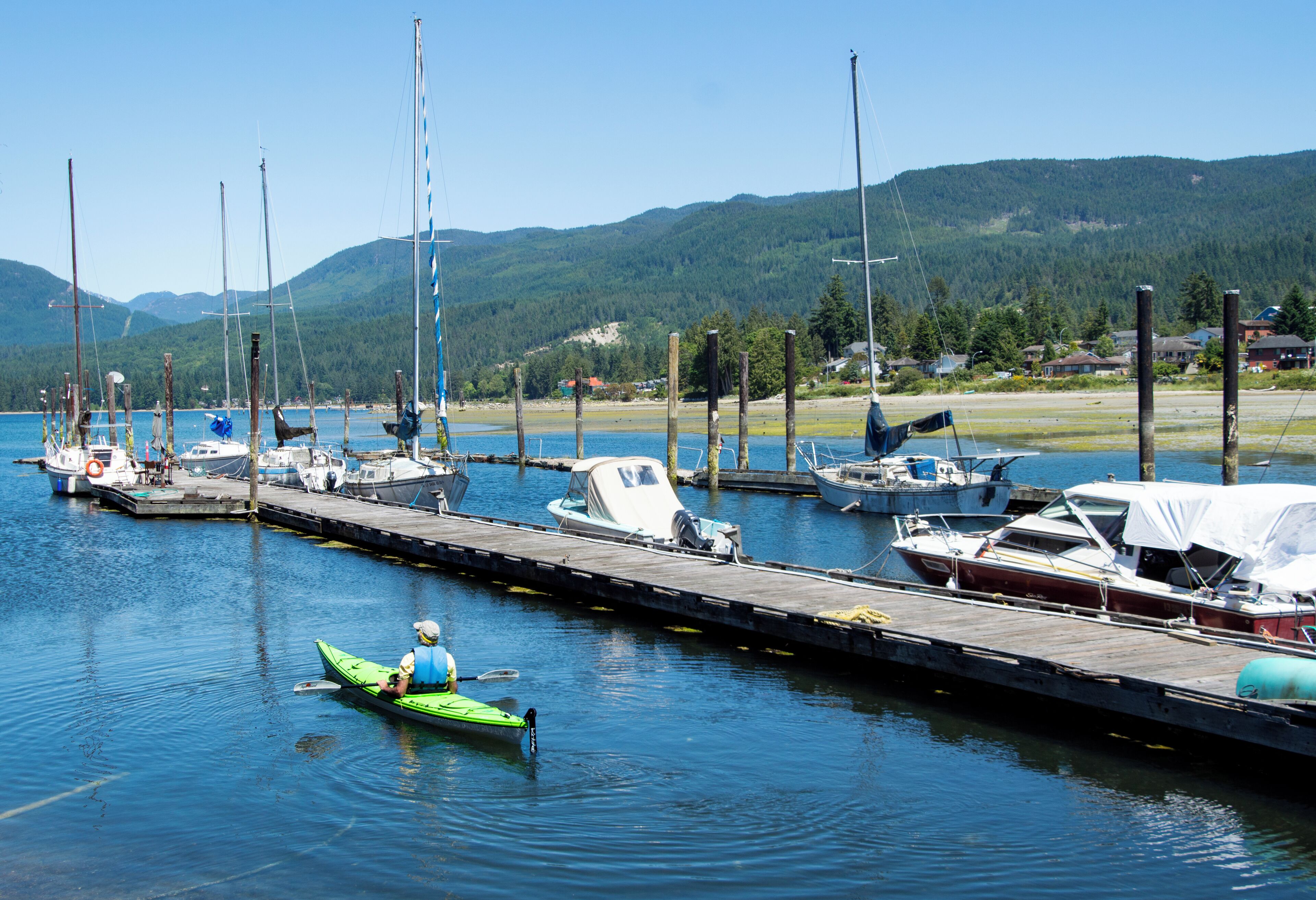 A marina with boats docked at wooden piers, surrounded by a forested landscape.