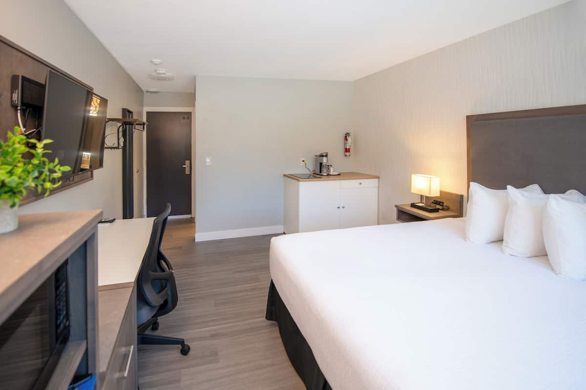 Habitación de hotel con cama, escritorio, silla, televisor y una kitchenette pequeña.