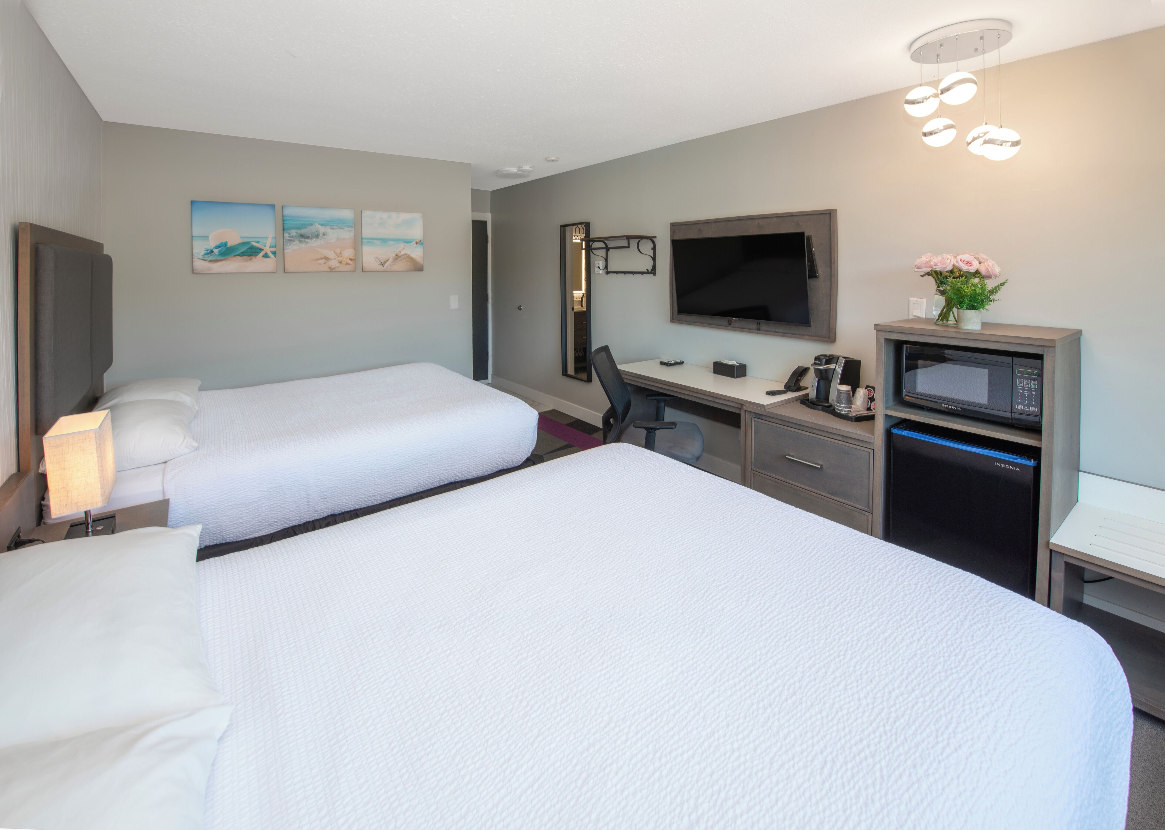 A hotel room with two beds, a desk, a television, a microwave, and a small plant.