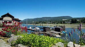 A marina with boats docked, a house with a dock, and a mountain in the background. - The Spot at Porpoise Bay (Sechelt)