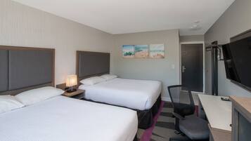 A hotel room with two beds, a desk, a chair, a TV, and artwork on the wall.