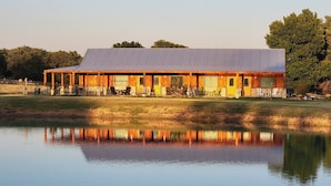 Un bâtiment en bois surmonté d’un toit métallique, dont le reflet se mire dans une étendue d’eau calme.