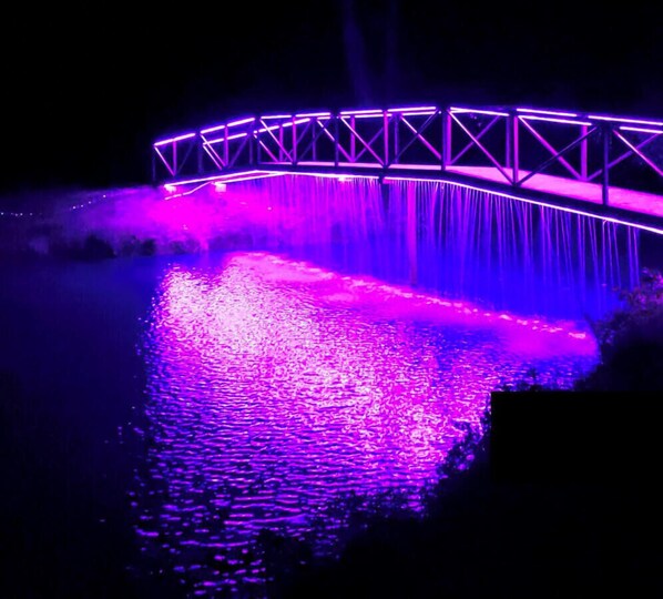Un pont illuminé de lumières violettes, surplombant une étendue d’eau.