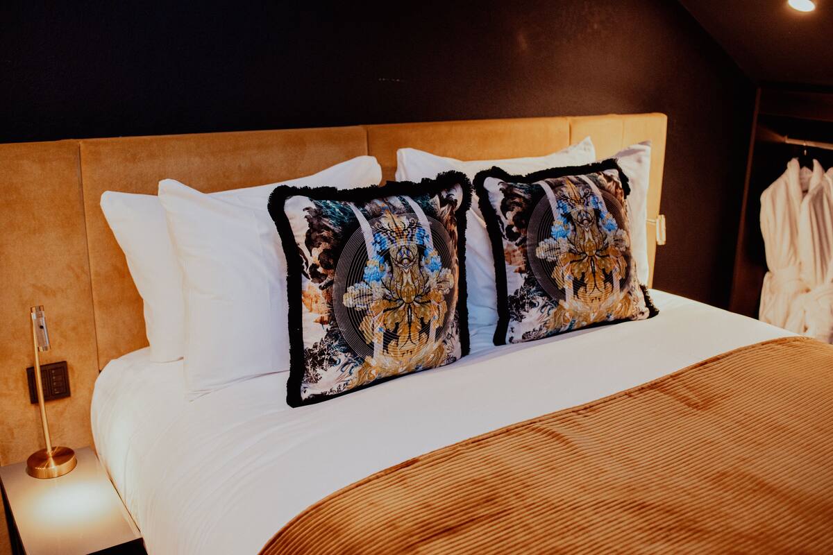 A hotel room with a large bed, two decorative pillows, a wooden headboard, and a robe hanging on the wall.
