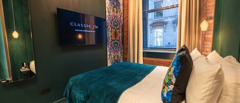 Quarto de hotel moderno com uma cama grande, uma televisão de tela plana, uma tapeçaria decorativa e vista para um edifício pela janela.