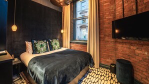 Une chambre d’hôtel moderne avec un grand lit, une télévision, un mur en briques et une fenêtre avec des rideaux.