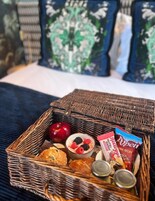 Una cesta de mimbre llena de alimentos sobre una cama con almohadones estampados.