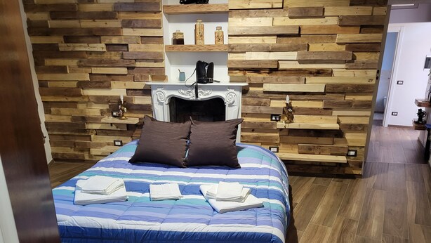Un dormitorio con pared de madera, una cama con ropa de cama azul y blanca, y una chimenea blanca.
